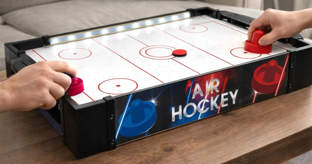 Two players using red mallets to play air hockey on a table